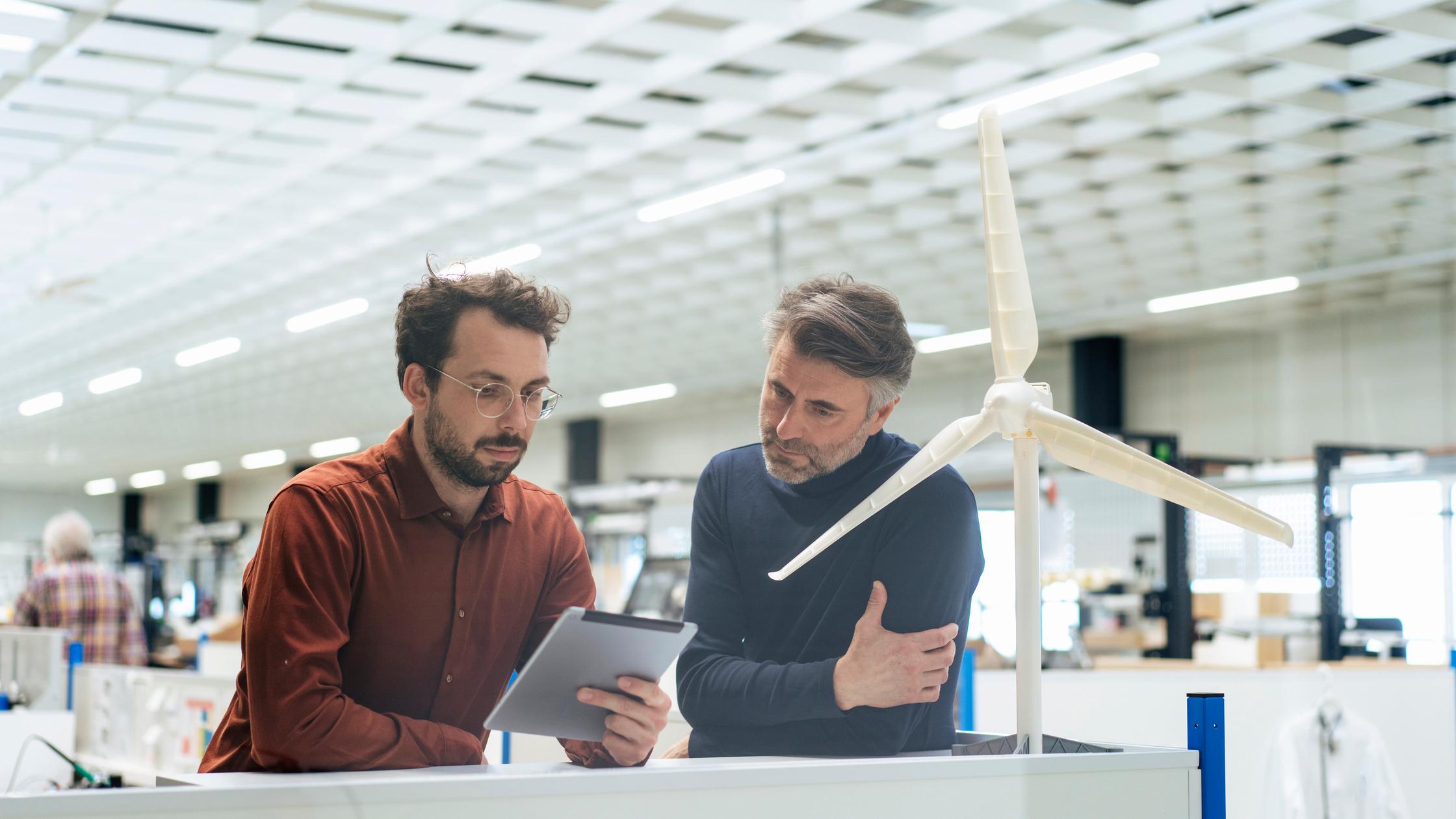 Two men looking at a digital tablet in a bright white room with turbine model in foreground