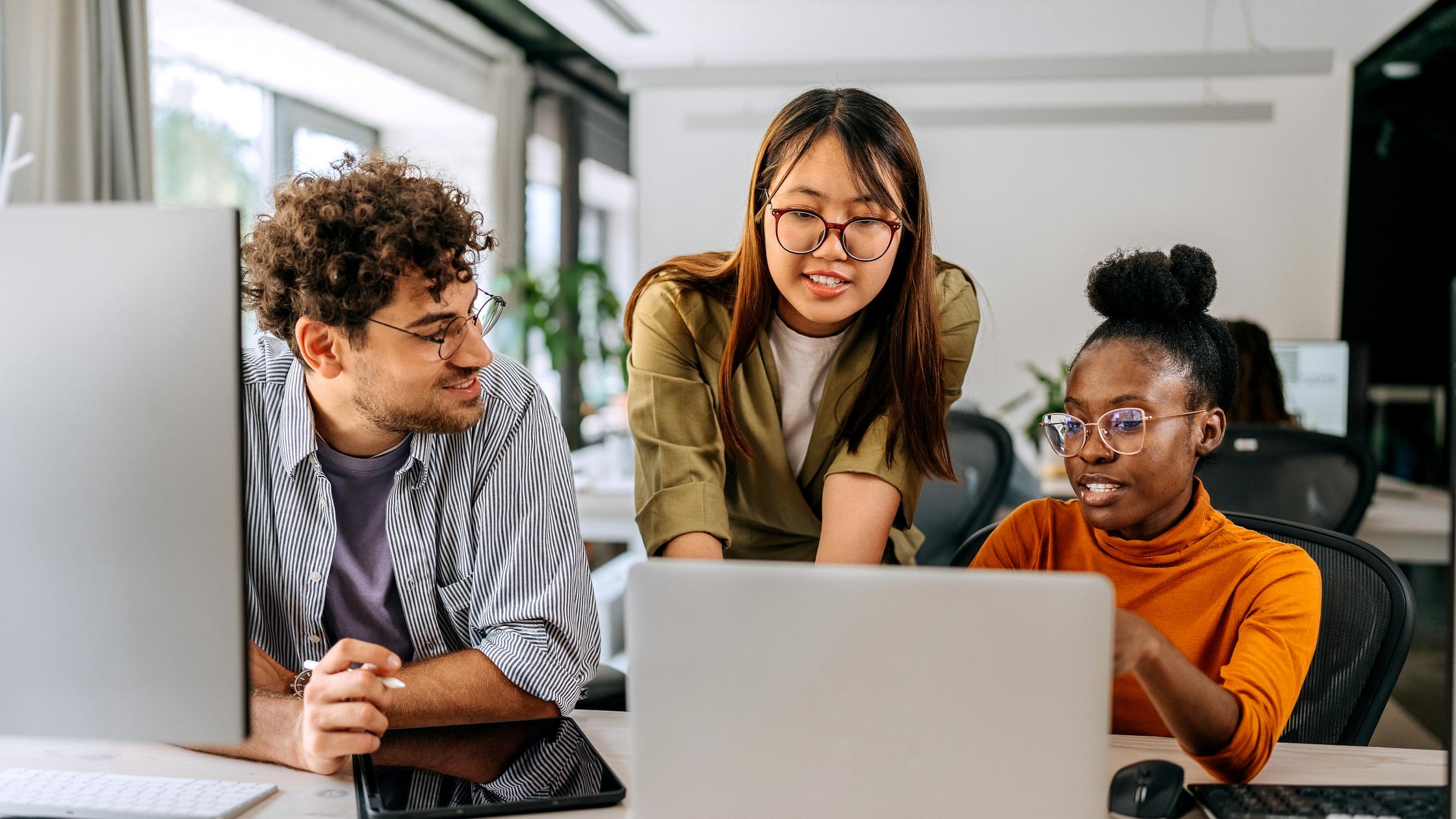 Three coworkers gathered around a laptop